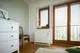 Weißes Elektroheizgerät an Wand unter Fenster, daneben eine Holzstuhl und eine Kommode. Helle, minimalistische Raumgestaltung mit Holzdetails und Rollladenfenstern. Vaillant Heizlösung.